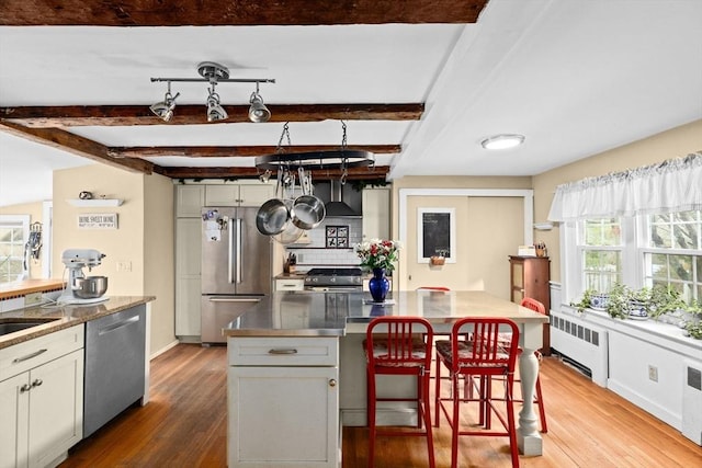 kitchen featuring radiator, beamed ceiling, wood finished floors, and stainless steel appliances