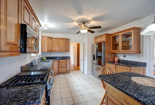 kitchen featuring light tile patterned floors, dark stone counters, a sink, stainless steel appliances, and glass insert cabinets