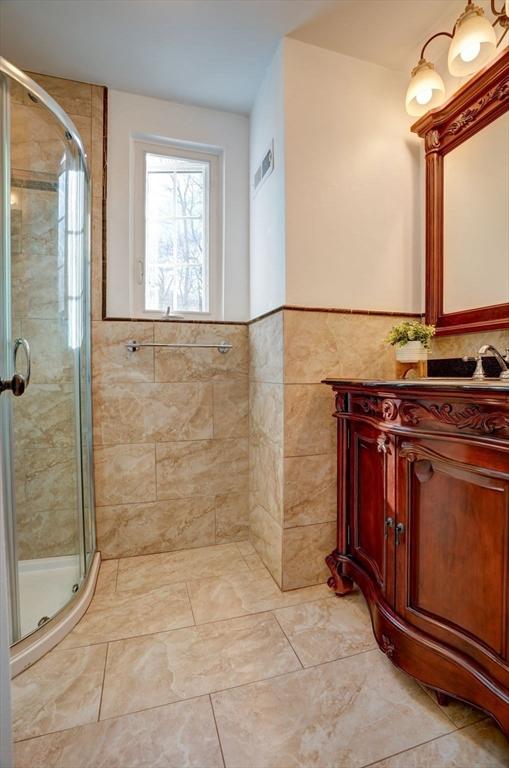 bathroom with visible vents, tile walls, a stall shower, and vanity