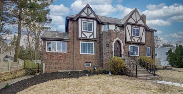 english style home with fence, brick siding, and a chimney