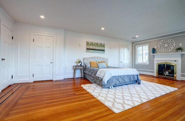 bedroom featuring crown molding, a fireplace with flush hearth, wood finished floors, and recessed lighting