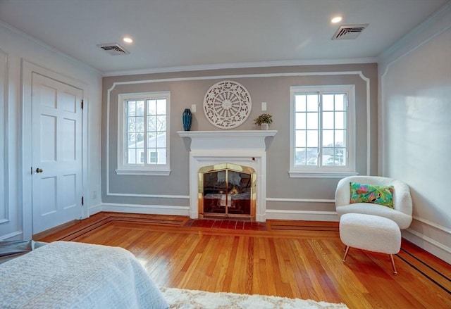 sitting room featuring visible vents, a fireplace with flush hearth, wood finished floors, and crown molding