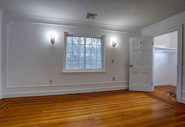 unfurnished room with visible vents, ornamental molding, light wood-style flooring, a textured ceiling, and baseboards