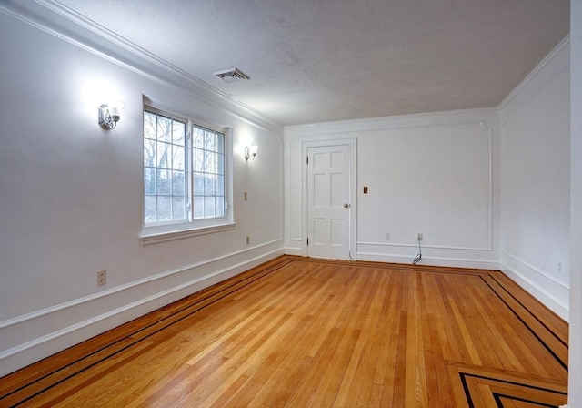 spare room featuring visible vents, ornamental molding, baseboards, and wood finished floors