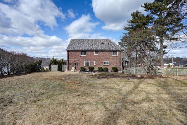 rear view of property with a yard, fence, and brick siding