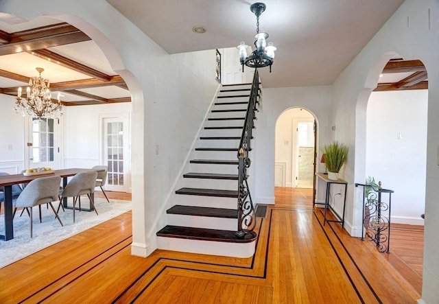 foyer entrance with arched walkways, a notable chandelier, beam ceiling, and hardwood / wood-style floors