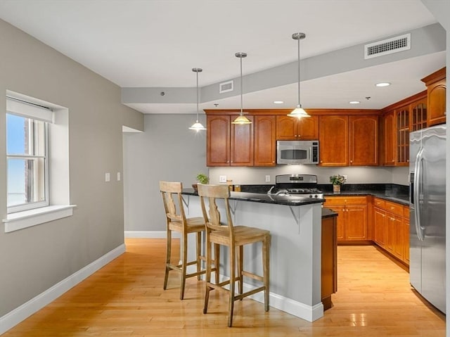 kitchen featuring light hardwood / wood-style flooring, appliances with stainless steel finishes, decorative light fixtures, a kitchen island, and a breakfast bar area