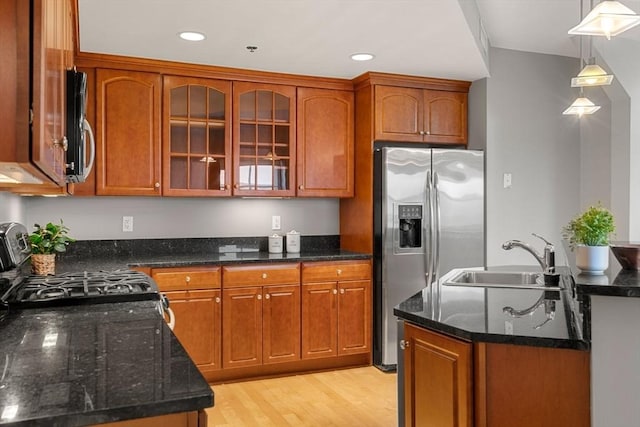 kitchen with pendant lighting, dark stone counters, sink, light hardwood / wood-style floors, and stainless steel appliances