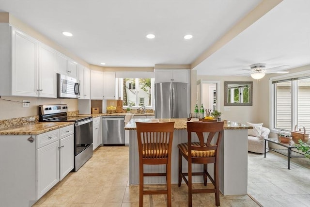 20 Chandler Rd, Andover, MA 01810 - kitchen featuring appliances with stainless steel finishes, a kitchen island, white cabinets, a kitchen bar, and light stone countertops