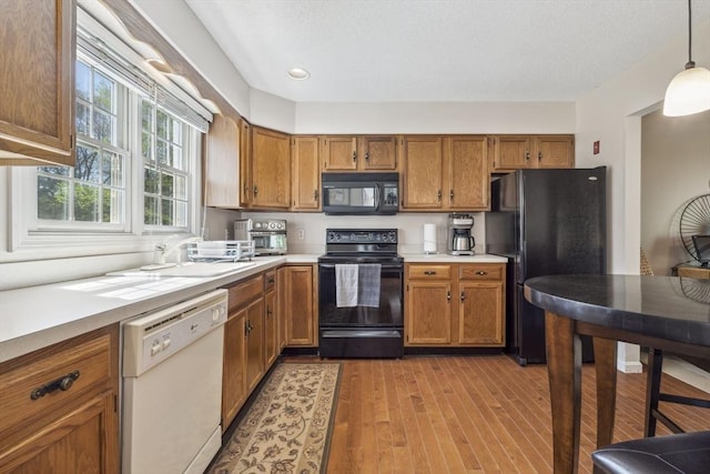 kitchen featuring brown cabinetry, light countertops, black appliances, and light wood-type flooring