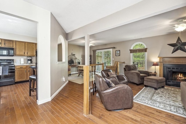 living area featuring a lit fireplace, a ceiling fan, and wood finished floors