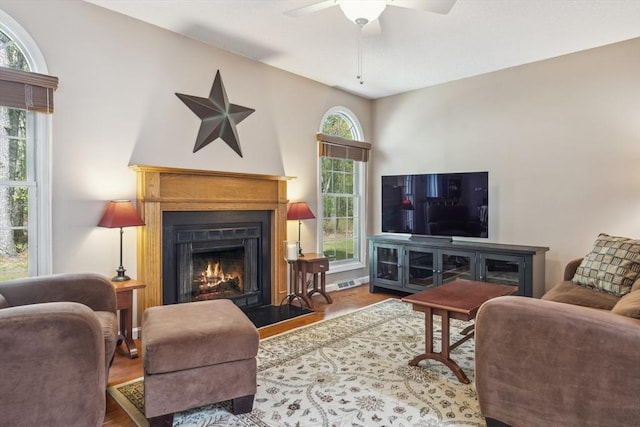 living room with a ceiling fan, a fireplace with flush hearth, wood finished floors, and visible vents