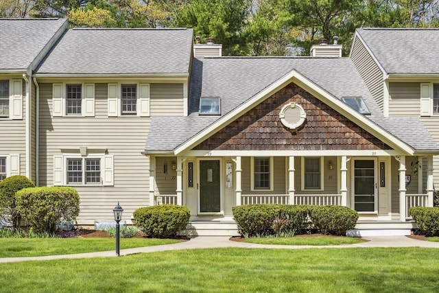 view of front of house with a porch, roof with shingles, a front yard, and a chimney