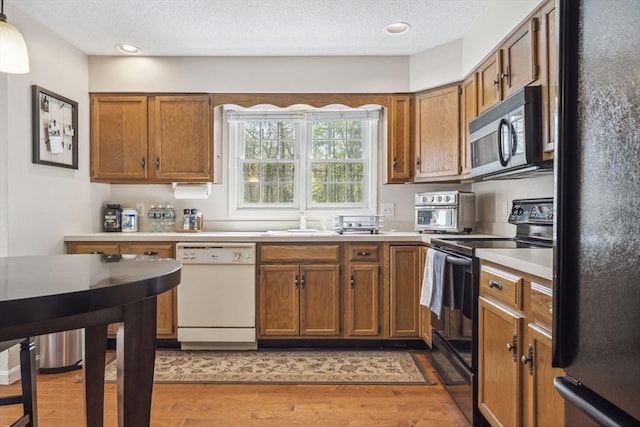 kitchen with light countertops, brown cabinetry, black appliances, and light wood-style floors