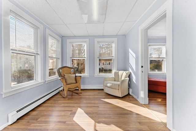 living area featuring baseboard heating, a wealth of natural light, a drop ceiling, and wood-type flooring