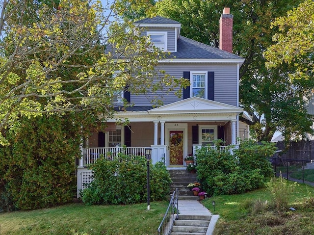 american foursquare style home with a shingled roof, a front lawn, a porch, stairs, and a chimney