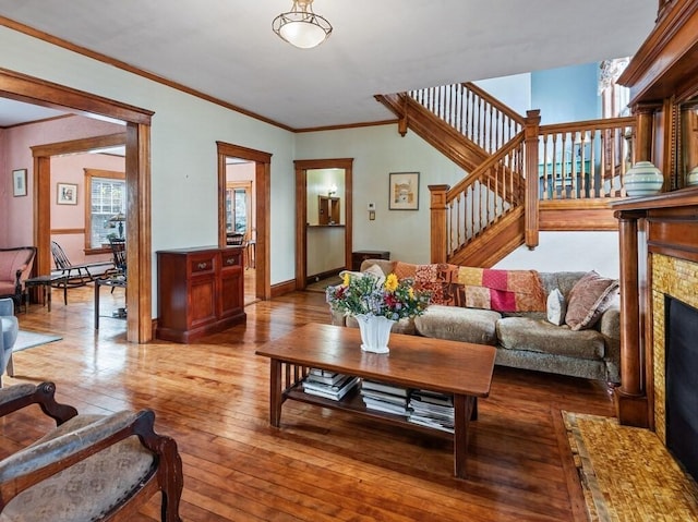 living room featuring baseboards, stairs, ornamental molding, a fireplace, and wood-type flooring