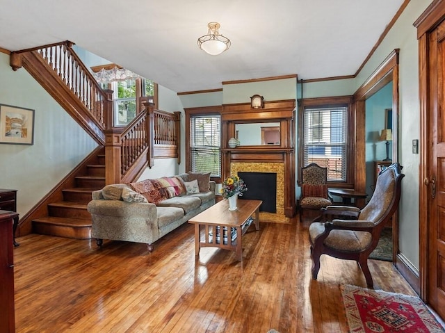 living area with stairway, a fireplace, crown molding, and wood-type flooring