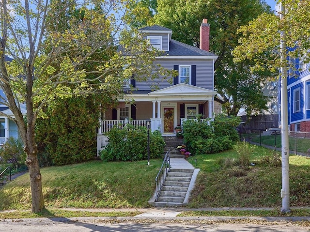 american foursquare style home with stairway, covered porch, a chimney, and a front yard