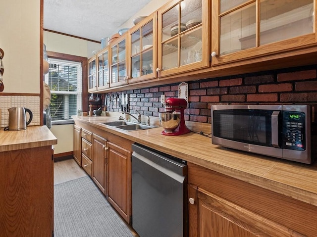 kitchen with wooden counters, decorative backsplash, brown cabinetry, stainless steel appliances, and a sink