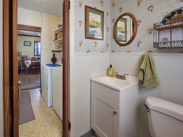 bathroom with wainscoting, wallpapered walls, toilet, and separate washer and dryer