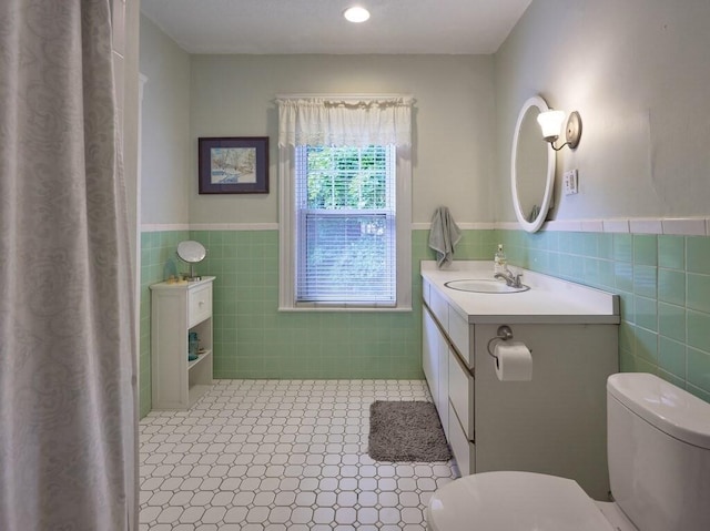 bathroom with tile walls, toilet, and a wainscoted wall