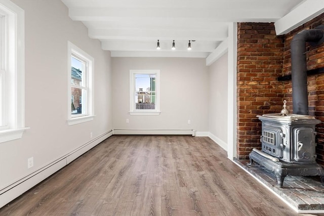 unfurnished living room with beamed ceiling, a baseboard heating unit, a wood stove, and light wood-type flooring