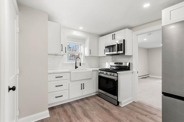 kitchen featuring sink, white cabinetry, light hardwood / wood-style flooring, baseboard heating, and appliances with stainless steel finishes