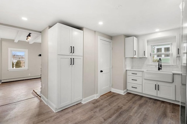 kitchen with baseboard heating, sink, hardwood / wood-style floors, and white cabinets