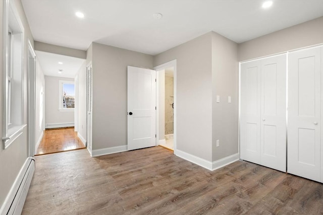 unfurnished bedroom featuring hardwood / wood-style flooring, a baseboard radiator, and a closet