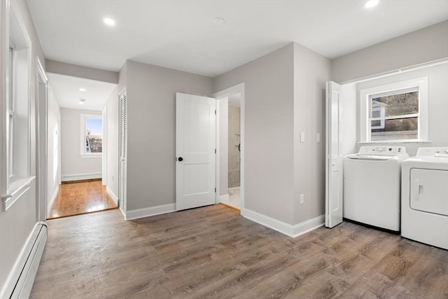 clothes washing area with wood-type flooring, washing machine and clothes dryer, and baseboard heating