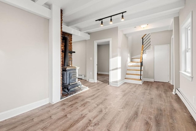 unfurnished living room with beamed ceiling, a baseboard heating unit, light wood-type flooring, and a wood stove