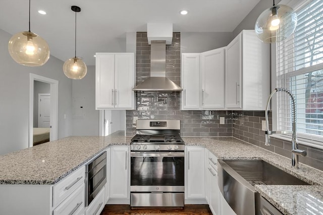 kitchen with wall chimney range hood, decorative backsplash, sink, white cabinetry, and stainless steel appliances