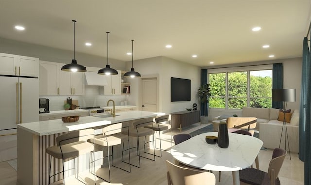 kitchen featuring high end white refrigerator, a kitchen island with sink, a sink, white cabinetry, and tasteful backsplash