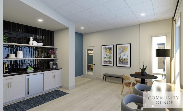 bar featuring baseboards, light wood-style flooring, a drop ceiling, a sink, and high end refrigerator