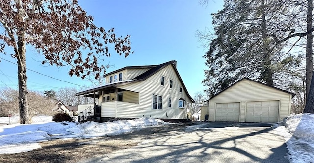 view of snow covered exterior with a garage, covered porch, and an outdoor structure