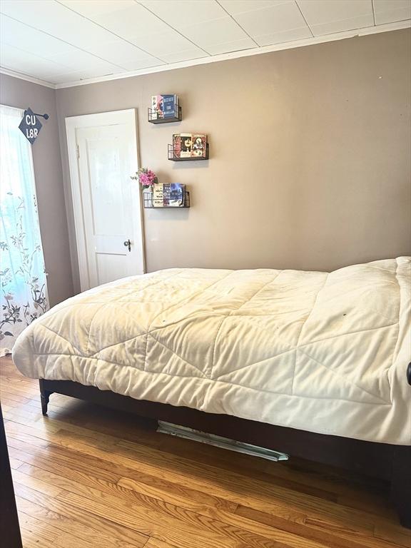 bedroom with ornamental molding and wood finished floors