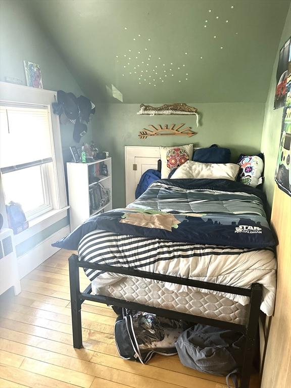 bedroom featuring lofted ceiling, radiator heating unit, and wood finished floors