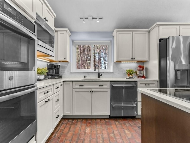 kitchen with light stone counters, a sink, white cabinets, appliances with stainless steel finishes, and backsplash