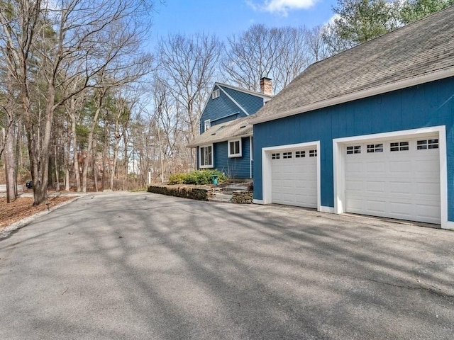 view of home's exterior with roof with shingles, driveway, and a chimney