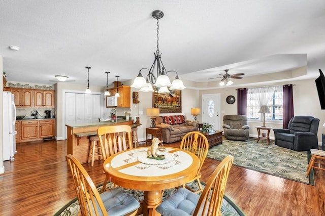 dining area featuring dark wood-style floors, ceiling fan with notable chandelier, and baseboards