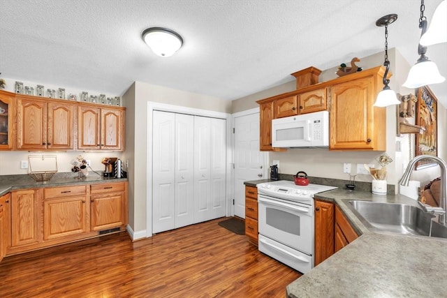 kitchen with brown cabinets, dark countertops, hanging light fixtures, a sink, and white appliances