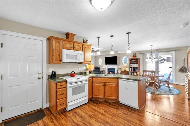 kitchen with white appliances, decorative light fixtures, a peninsula, a lit fireplace, and light wood-style floors