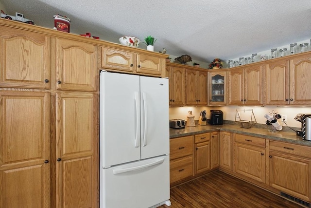 kitchen with dark wood-style flooring, dark countertops, glass insert cabinets, freestanding refrigerator, and a textured ceiling