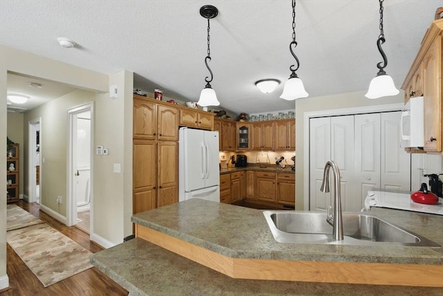 kitchen featuring white appliances, dark countertops, glass insert cabinets, decorative light fixtures, and a sink