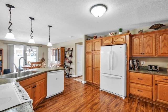 kitchen with white appliances, a sink, brown cabinets, dark countertops, and pendant lighting