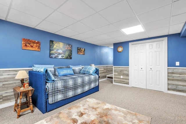 bedroom featuring a wainscoted wall, a paneled ceiling, a closet, carpet flooring, and wooden walls