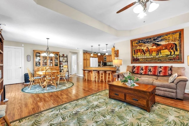 living area with ceiling fan with notable chandelier, light wood-type flooring, and baseboards