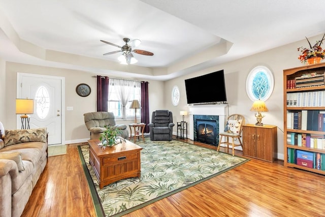 living room featuring a high end fireplace, a tray ceiling, ceiling fan, and wood finished floors