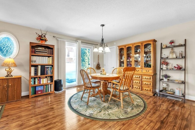 dining space featuring a notable chandelier, a textured ceiling, baseboards, and wood finished floors